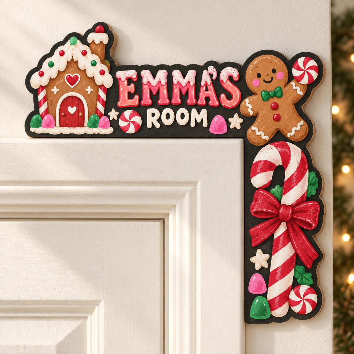 May include: A black L-shaped door corner sign featuring a gingerbread house on the left, a gingerbread person on the right, and a candy cane below. The text reads EMMA'S ROOM in pink and white lettering, accented with peppermint candies and gumdrops.