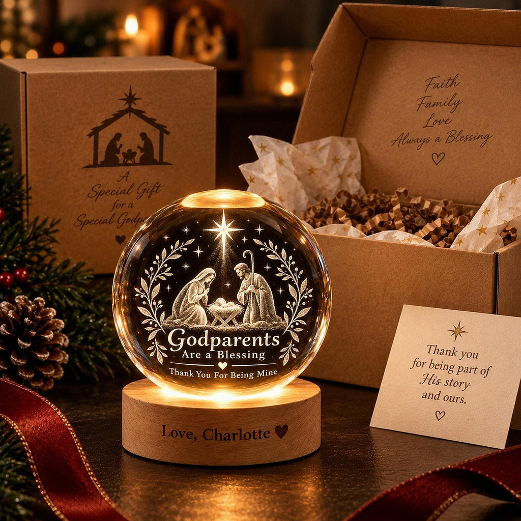 May include: A clear glass sphere engraved with a nativity scene and the text Godparents Are A Blessing, Thank You For Being Mine, resting on a round wooden base inscribed with Love, Charlotte, accompanied by a gift box and a note.