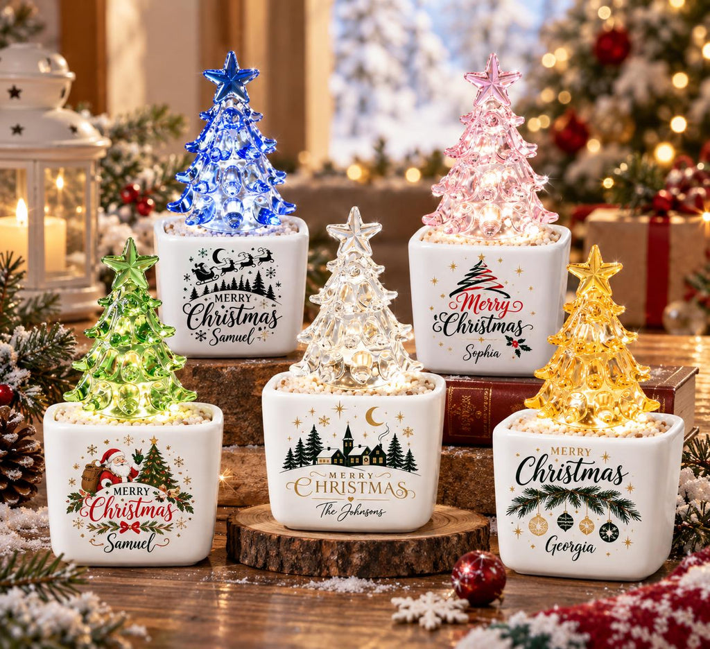 May include: Five square white ceramic planters, each containing a small, translucent, illuminated Christmas tree in blue, pink, green, clear, or yellow. Each planter features festive holiday graphics and personalized names or text.