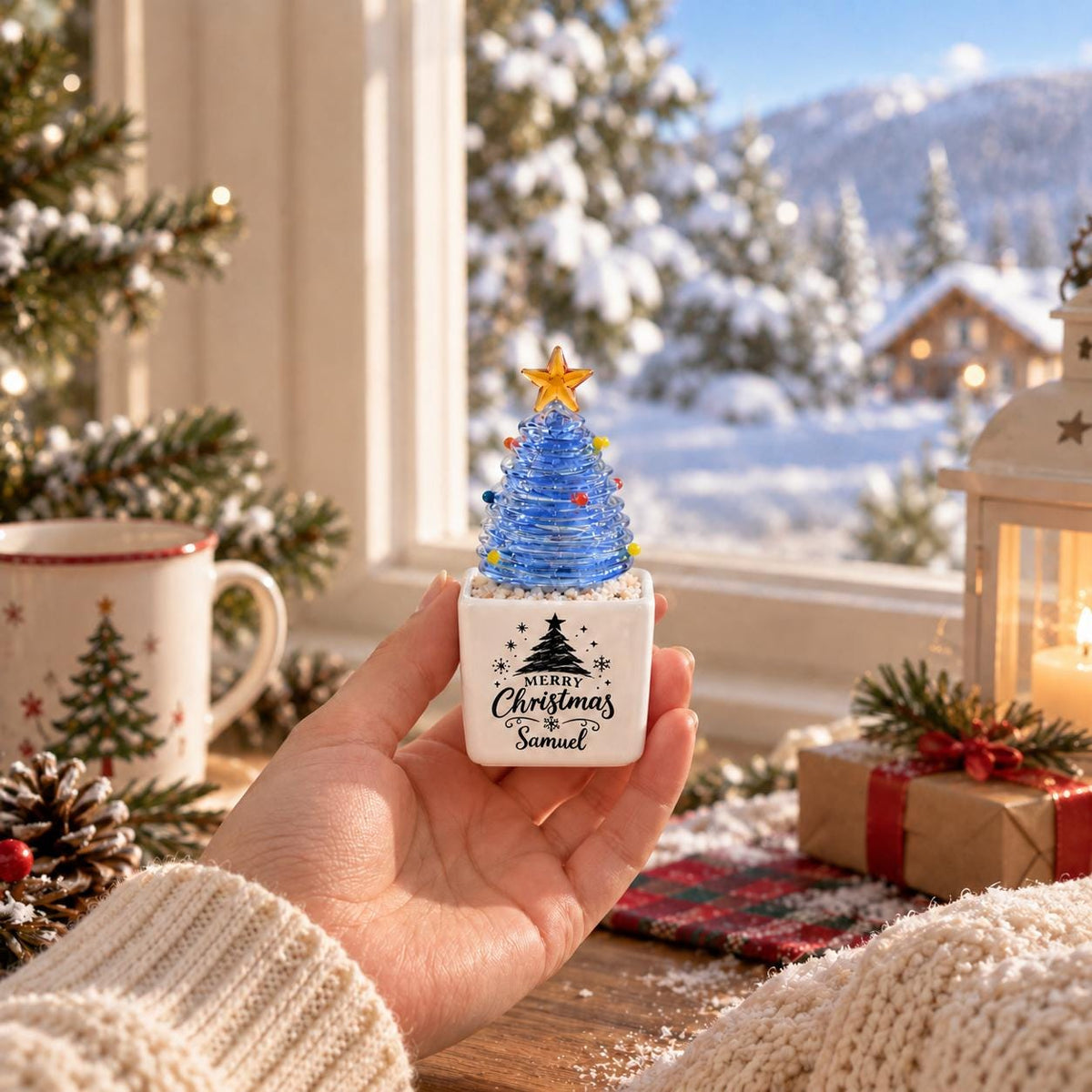 May include: A small blue glass Christmas tree ornament with a yellow star topper, set in a white square ceramic base. The base features a black printed graphic of a pine tree and the text Merry Christmas Samuel in a decorative script font.