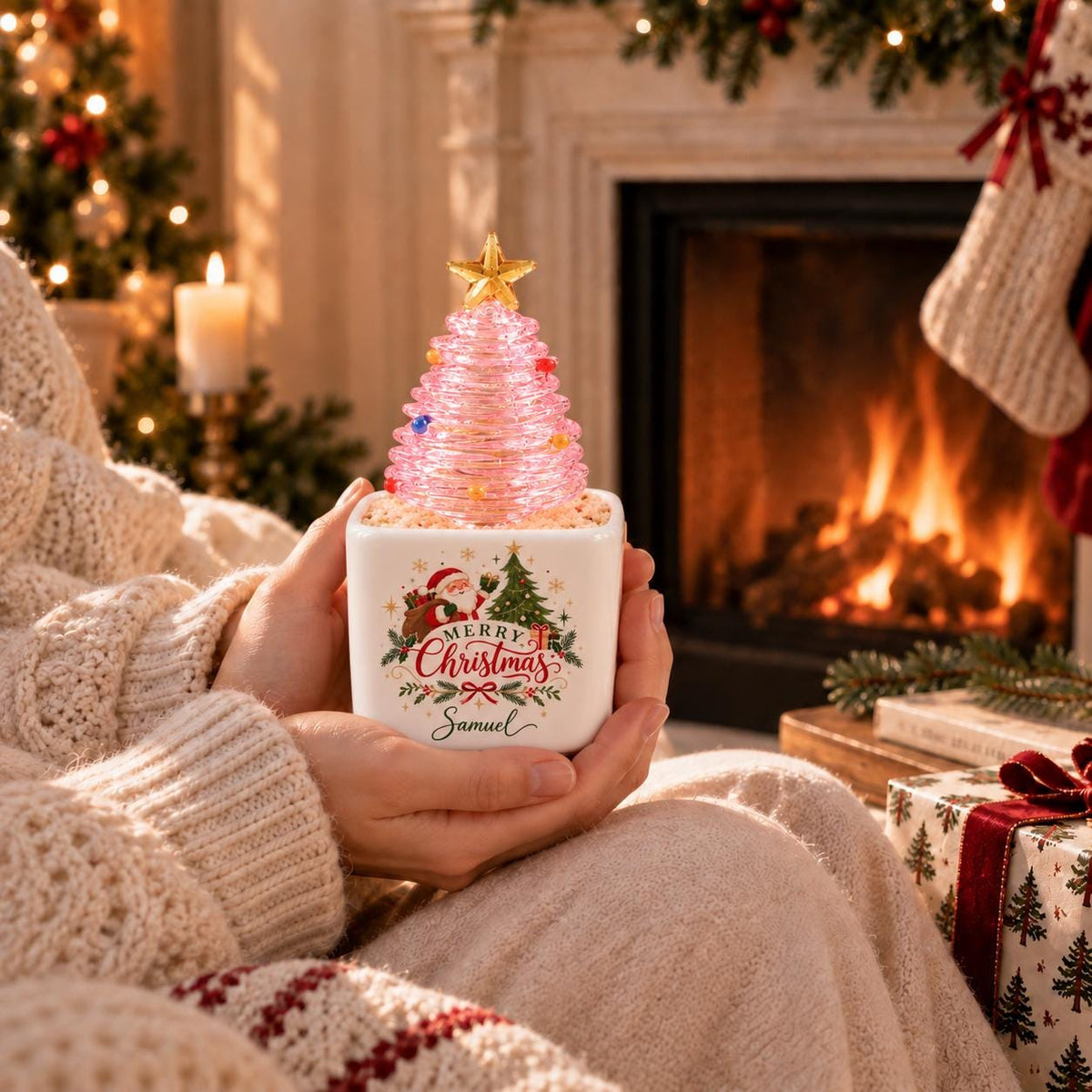 May include: A square white ceramic planter featuring a graphic of Santa Claus, a pine tree, and the text Merry Christmas Samuel. A translucent pink spiral-shaped Christmas tree ornament with a gold star topper sits inside the planter.