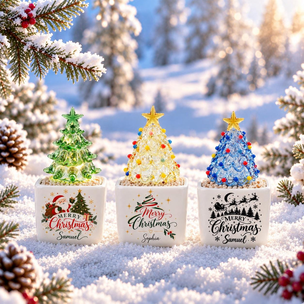 May include: Three glass Christmas tree figurines in square white ceramic pots. The trees are green, yellow, and blue with star toppers. Each pot features festive graphics and the names Samuel, Sophia, and Samuel printed in black and red text.