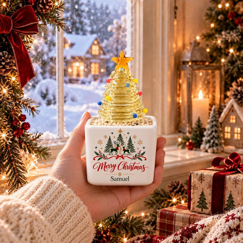 May include: A square white ceramic planter featuring a festive graphic of pine trees, reindeer, and the text Merry Christmas with the name Samuel printed below. A ribbed glass Christmas tree with small colorful bulbs sits on top.
