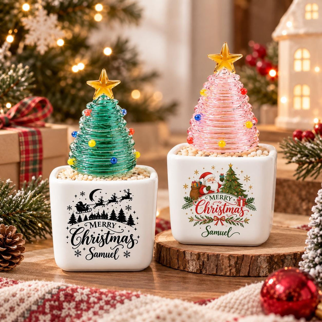 May include: Two square white ceramic planters featuring glass Christmas tree toppers with yellow stars. One planter displays black text reading Merry Christmas Samuel with a sleigh silhouette, while the other shows a colorful Santa graphic.