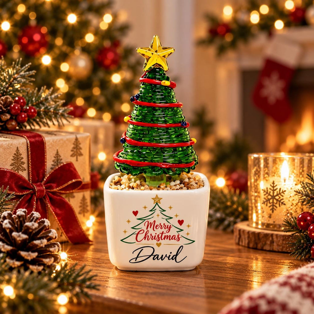 May include: A small decorative Christmas tree made of green wire with red garland and a yellow star topper, set in a white square ceramic planter. The planter features a printed green tree graphic, red hearts, and the text Merry Christmas David.