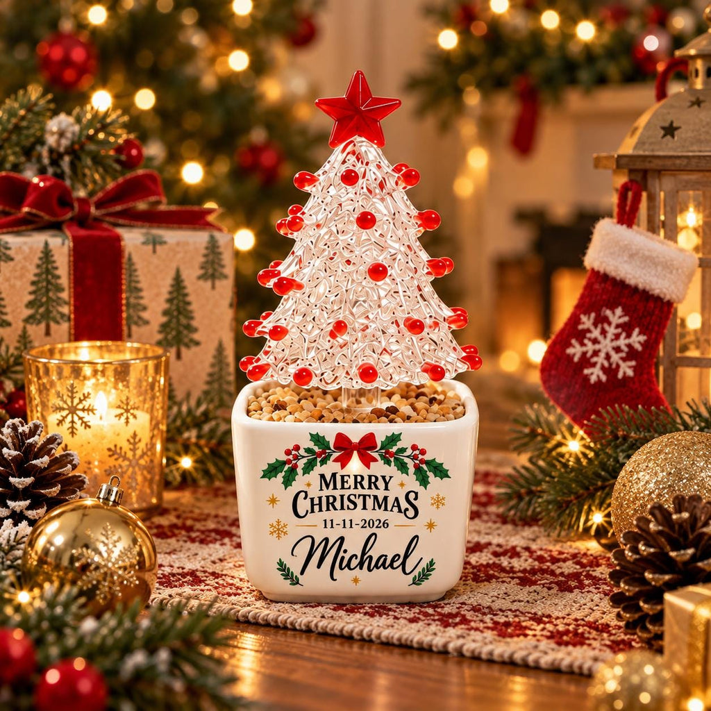 May include: A clear, textured glass Christmas tree ornament with red accents and a red star topper, set in a white square ceramic planter. The planter features a green holly design, the text Merry Christmas 11-11-2026, and the name Michael.