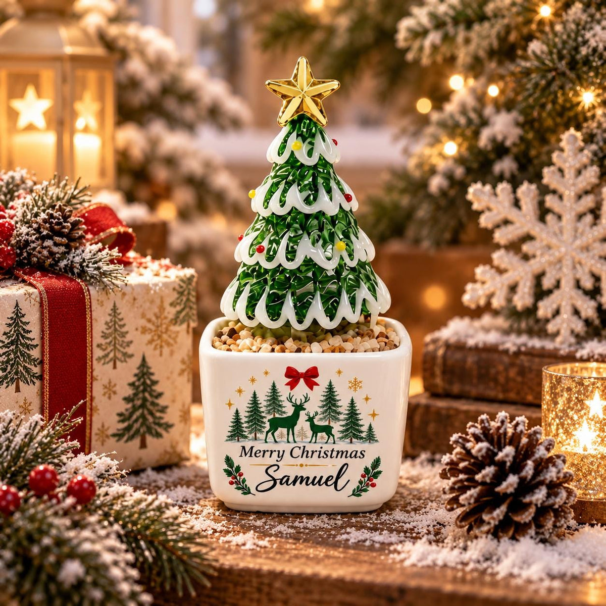 May include: A decorative Christmas tree figurine with green glass branches, white snow-like accents, and a gold star topper, set in a white square ceramic planter featuring a printed forest scene with deer and the text Merry Christmas Samuel.