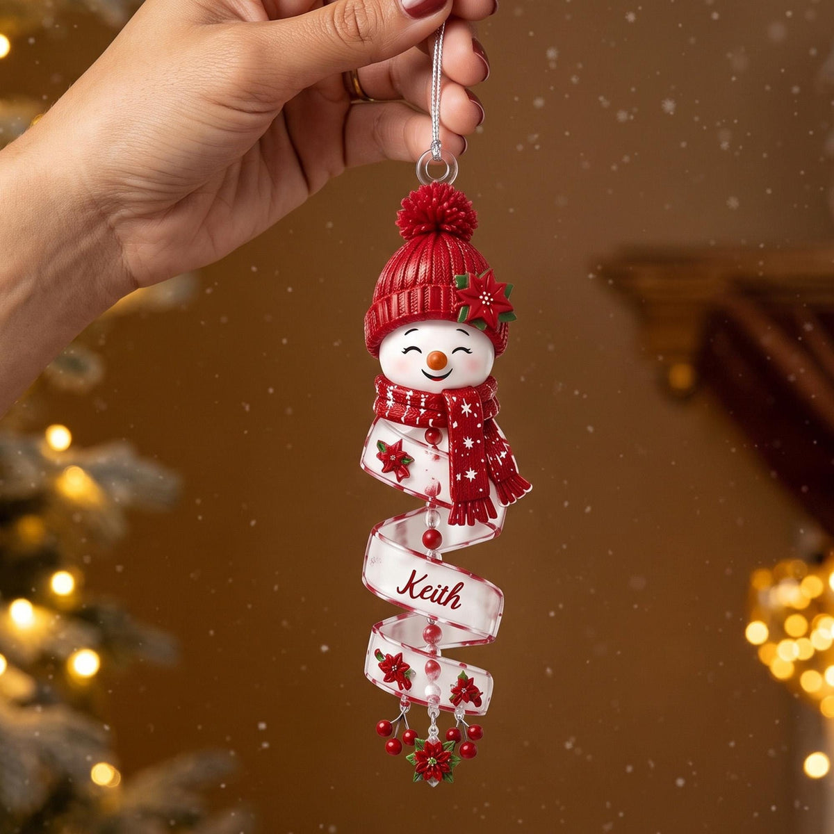 May include: A hanging Christmas ornament featuring a smiling snowman head wearing a red knit hat with a pom-pom and a matching red scarf. Below the snowman, a white spiral ribbon displays the name Keith and is decorated with red poinsettias.