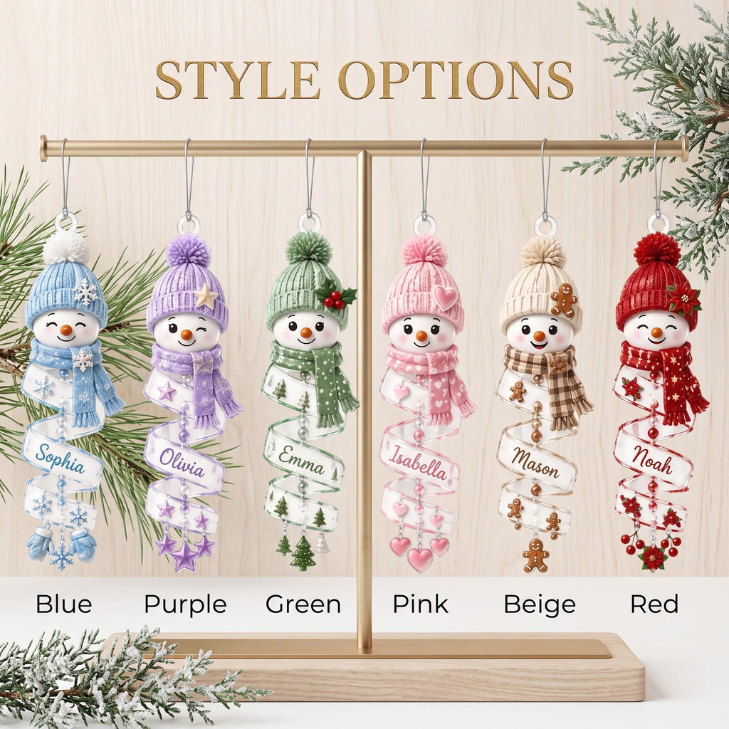 May include: Six hanging snowman ornaments in blue, purple, green, pink, beige, and red. Each snowman wears a matching knit hat and scarf, with a spiral ribbon base featuring names: Sophia, Olivia, Emma, Isabella, Mason, and Noah. Text reads STYLE OPTIONS.