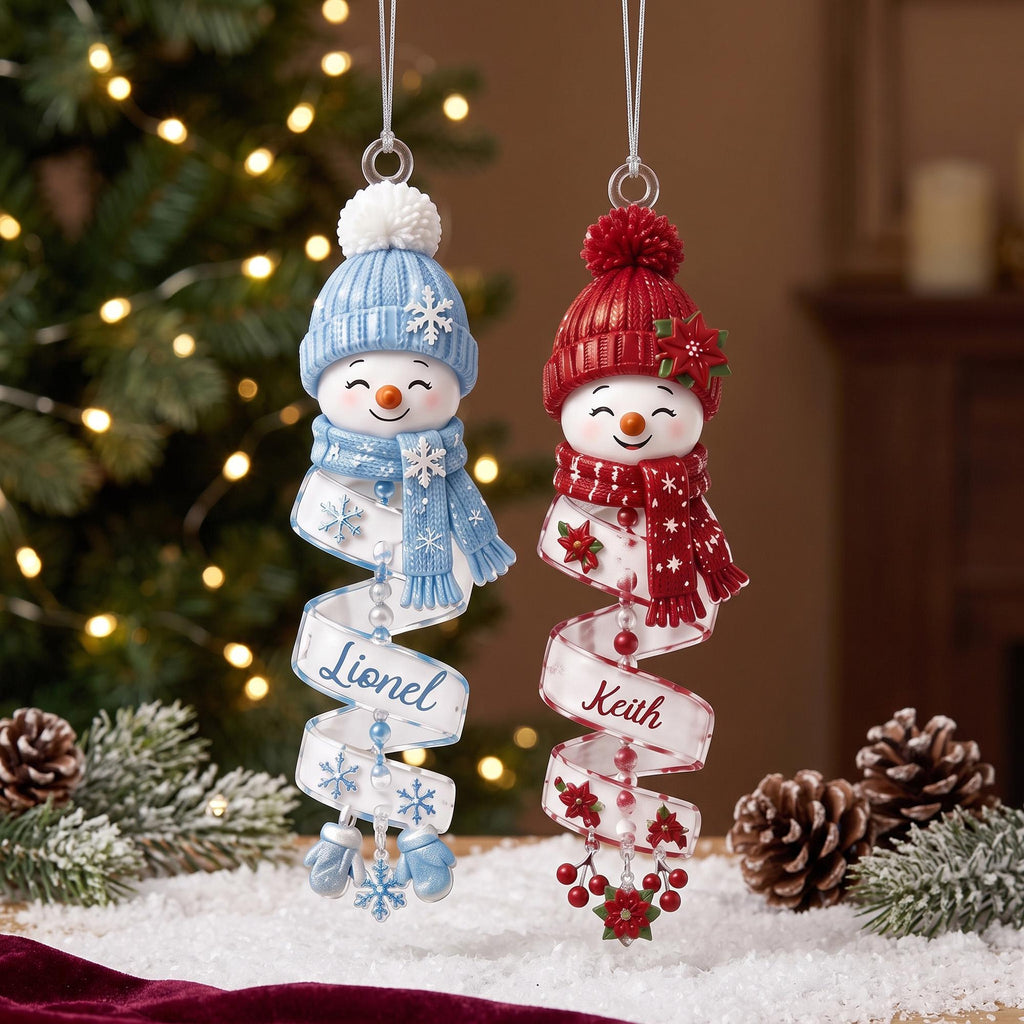 May include: Two hanging snowman ornaments with spiral ribbons. The left snowman wears a blue hat and scarf with snowflakes and the name Lionel. The right snowman wears a red hat and scarf with poinsettias and the name Keith. Both have white pom-poms.