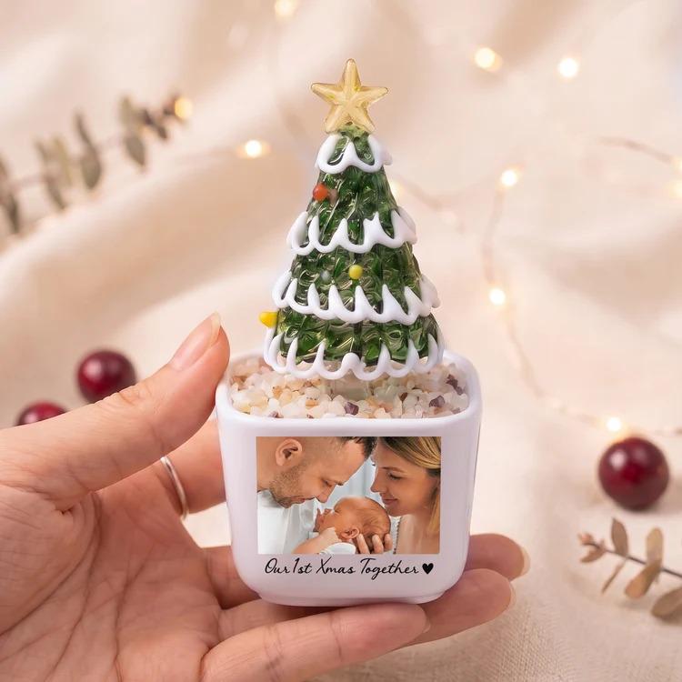 May include: A small white square planter containing a glass Christmas tree with white trim and a gold star topper. The planter features a printed photograph of a family and the text Our 1st Xmas Together with a small black heart icon.