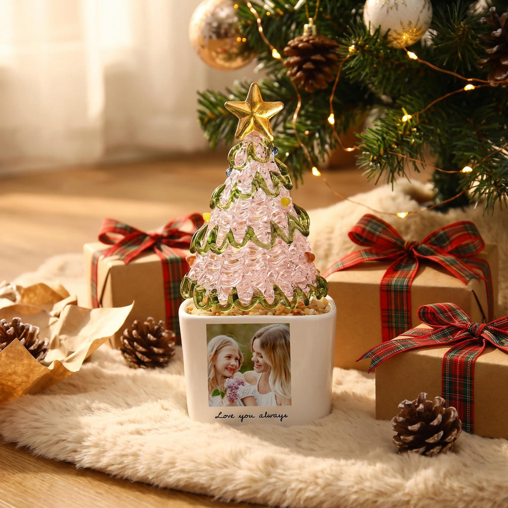 May include: A decorative glass Christmas tree with a pink textured body, green glass garland, and a gold star topper. The tree sits in a white square planter featuring a printed photograph of two people and the text Love you always.