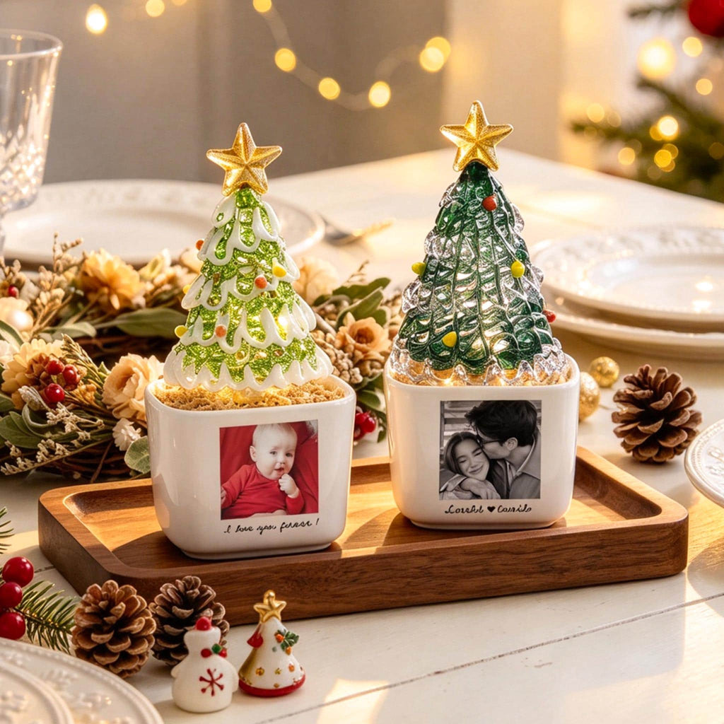 May include: Two square white ceramic planters featuring custom photo prints and text, each topped with a decorative glass Christmas tree with a gold star topper. The planters sit on a rectangular wooden tray, illuminated by internal lights.