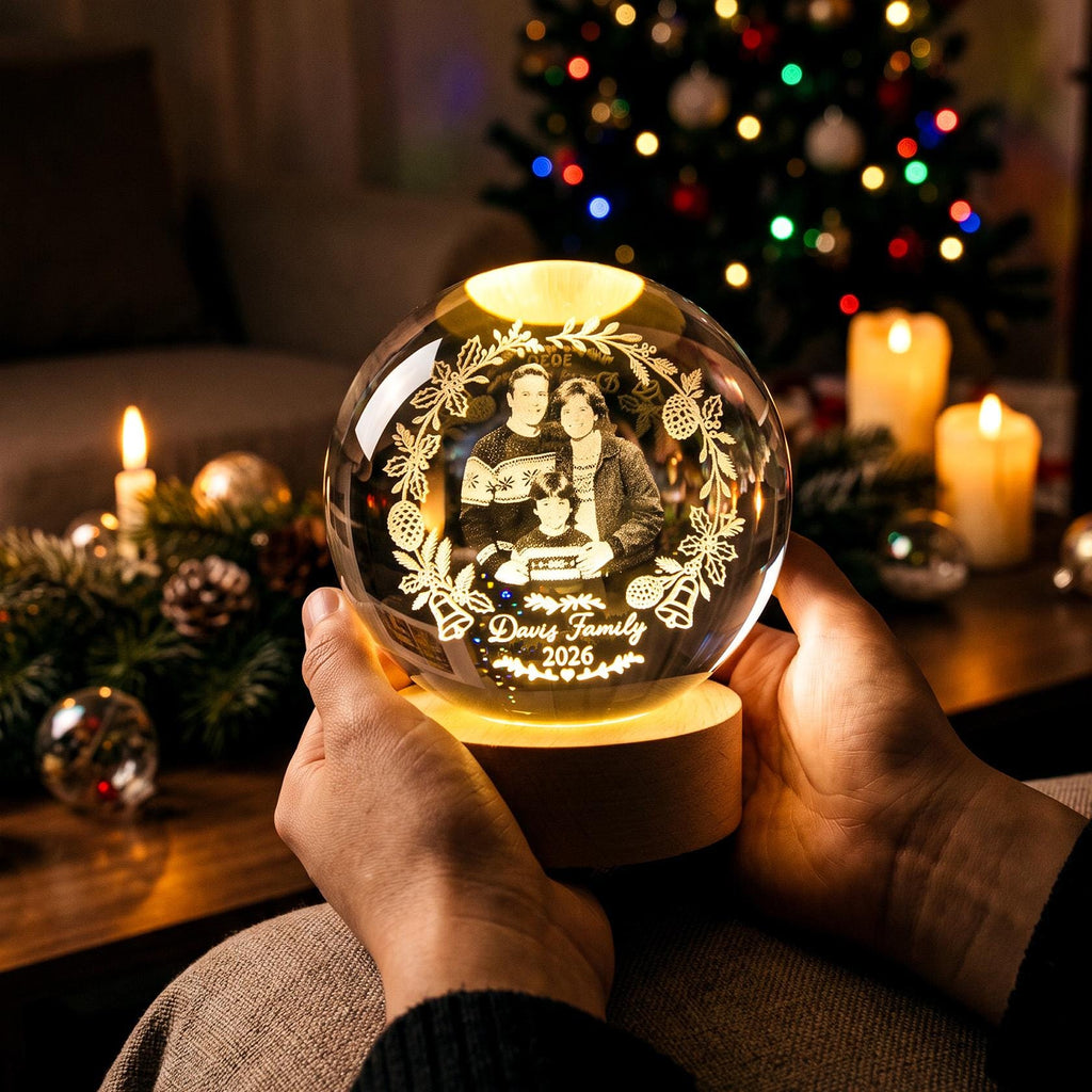 May include: A clear glass sphere featuring a laser-etched portrait of a family of three inside a decorative wreath. The text "Davis Family 2026" is engraved at the bottom. The sphere rests on a circular wooden base that illuminates the interior.