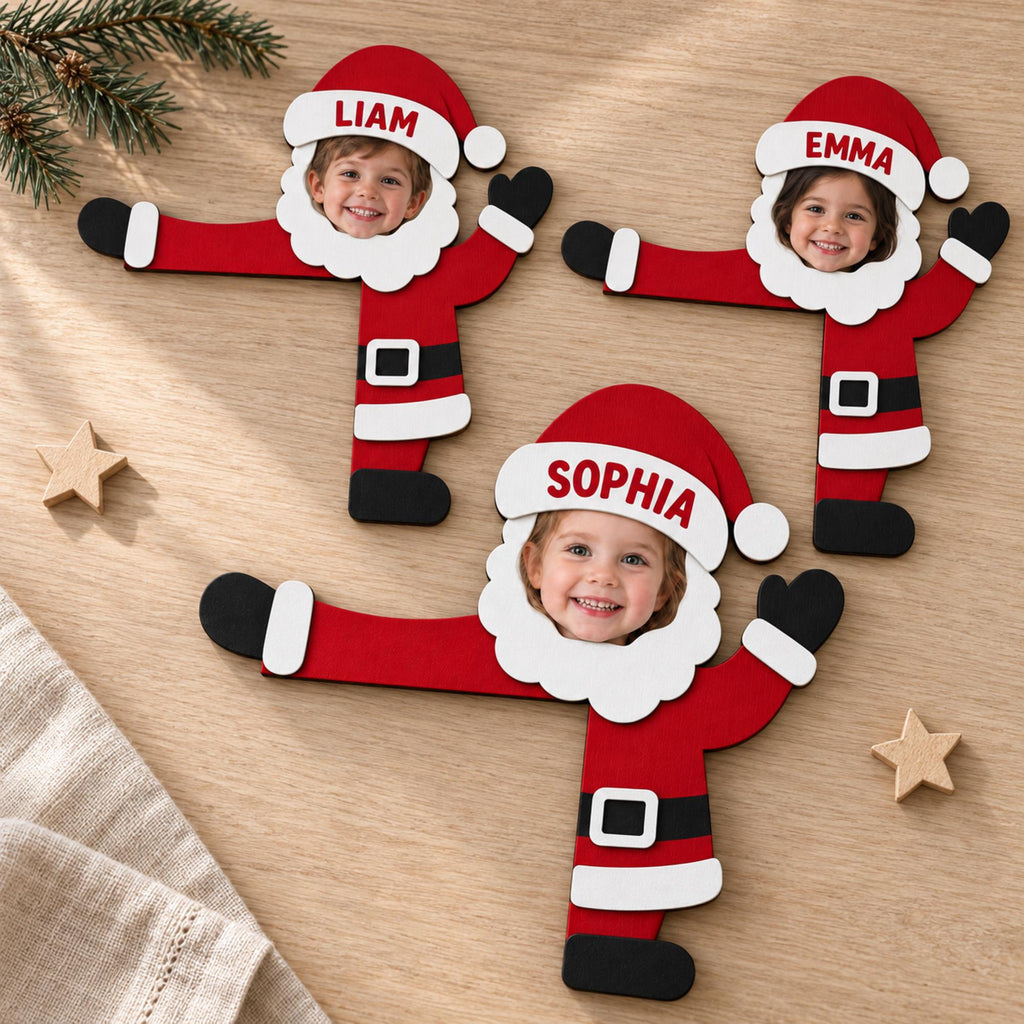 May include: Three flat wooden Santa Claus ornaments featuring cutout faces for personalized photos. Each Santa wears a red hat with the names Liam, Emma, or Sophia printed in red, a white beard, a red coat, a black belt with a white buckle, and black boots.