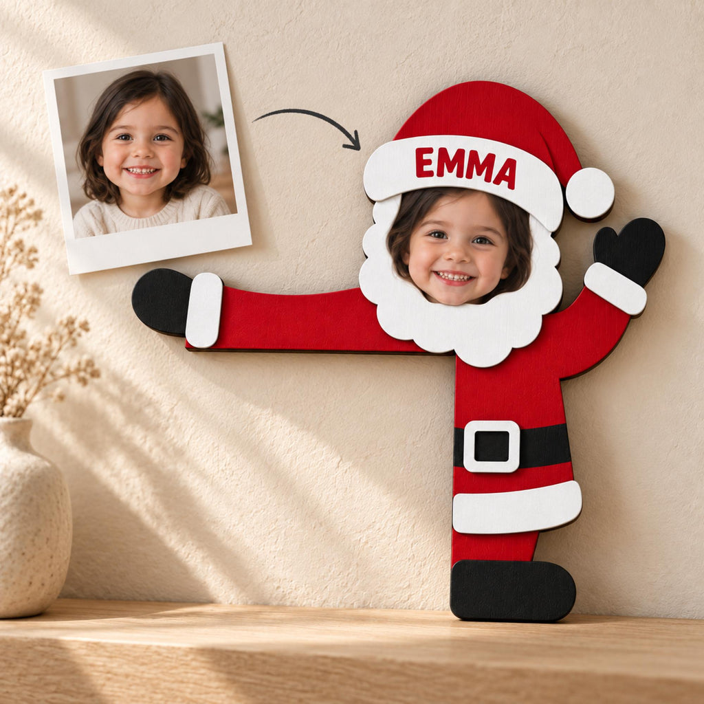 May include: A red and white wooden Santa Claus cutout with a cutout face area for a photo. The white hat brim features the name EMMA in red text. The figure includes black gloves and boots, a black belt with a white buckle, and a white beard.