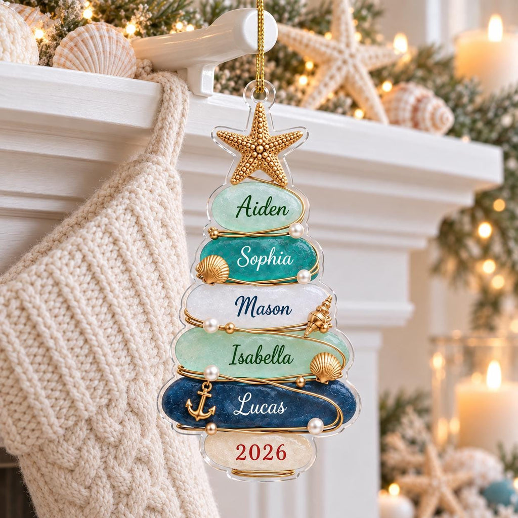 May include: A Christmas tree-shaped ornament made of stacked, smooth, multi-colored stones in shades of blue, green, and white. The ornament features a gold starfish topper, gold wire accents, small pearls, seashells, and an anchor charm. Names Aiden, Sophia, Mason, Isabella, Lucas, and the year 2026 are printed on the stones.