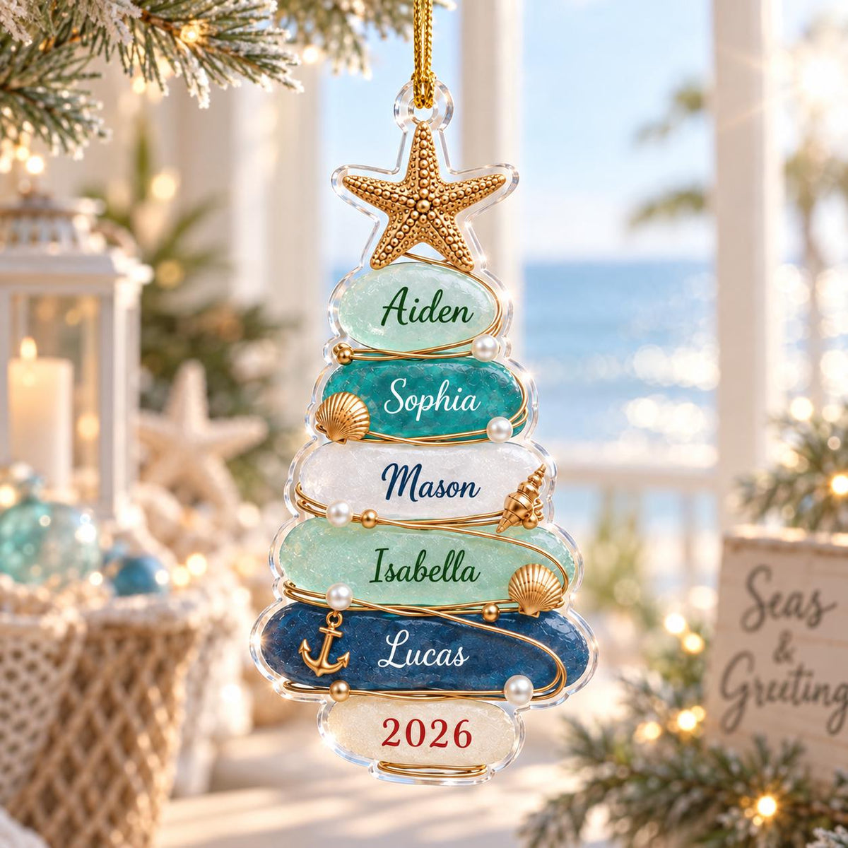 May include: A clear, tree-shaped Christmas ornament featuring stacked, textured glass-like layers in shades of blue, teal, and white. The ornament is topped with a gold starfish and decorated with small pearls, shells, and an anchor, with names and 2026 printed.