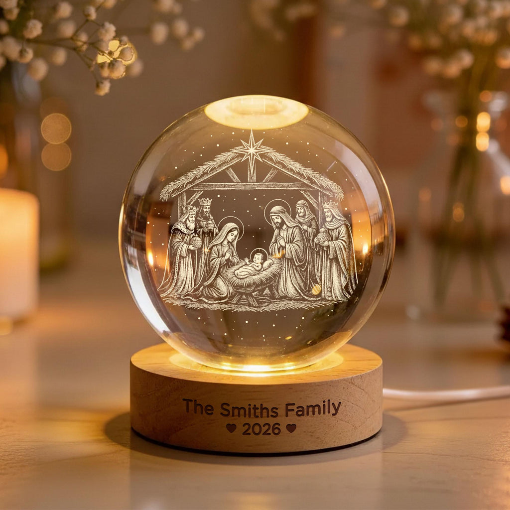 May include: A clear glass sphere featuring an internal laser-etched nativity scene with a star above a stable. The sphere rests on a circular light-colored wooden base engraved with the text The Smiths Family and the year 2026 with heart icons.