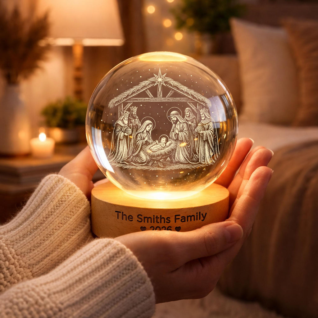 May include: A clear glass sphere featuring an internal laser-etched nativity scene with a star above. The sphere rests on a circular wooden base illuminated from below, with the text "The Smiths Family" and "2026" engraved on the front side.