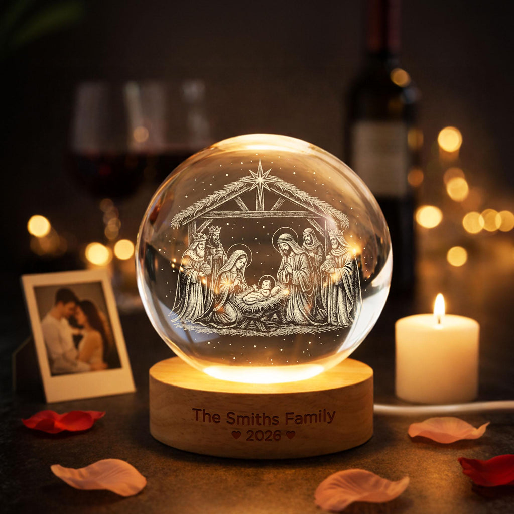 May include: A clear glass sphere featuring an internal laser-etched nativity scene with a star above. The sphere rests on a cylindrical wooden base engraved with the text "The Smiths Family" followed by "2026" and two small heart symbols.