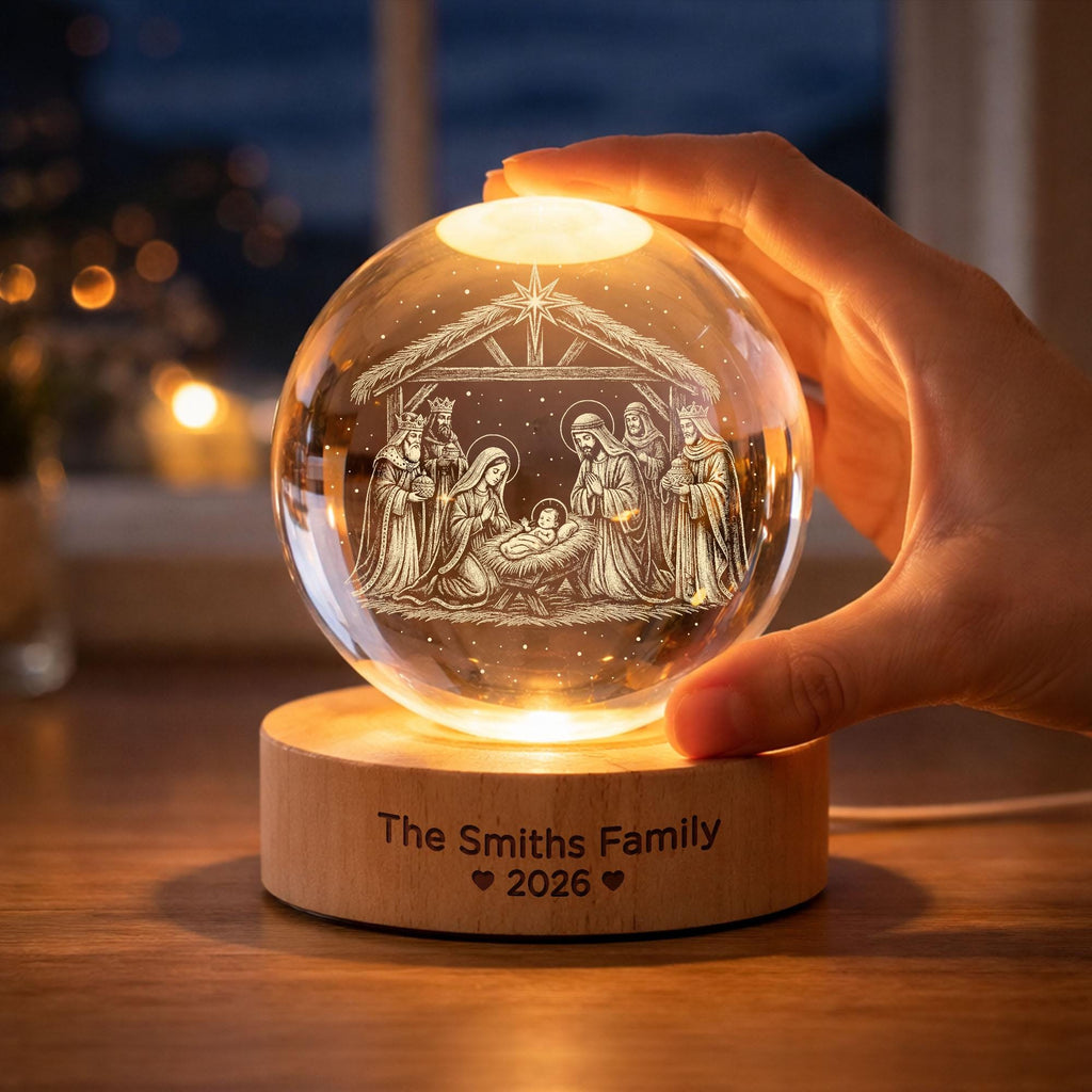 May include: A clear glass sphere featuring an internal laser-etched nativity scene with a star above. The sphere rests on a cylindrical wooden base illuminated from below, engraved with the text The Smiths Family and the year 2026 with hearts.