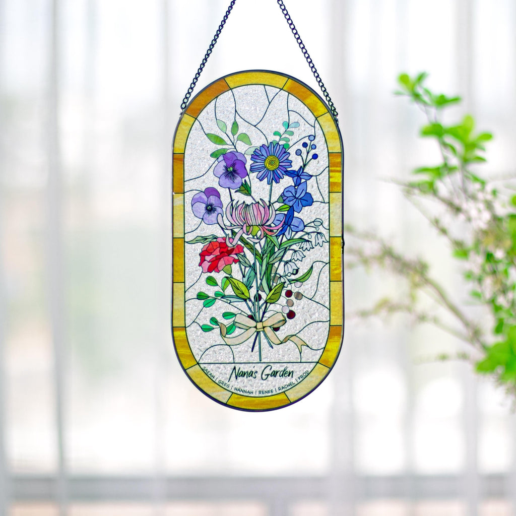 May include: Stained glass window art featuring a bouquet of colorful flowers in shades of red, purple, blue, and pink. The oval-shaped panel has a yellow border and is suspended by a black chain. The text "Nana's Garden" is visible at the bottom.