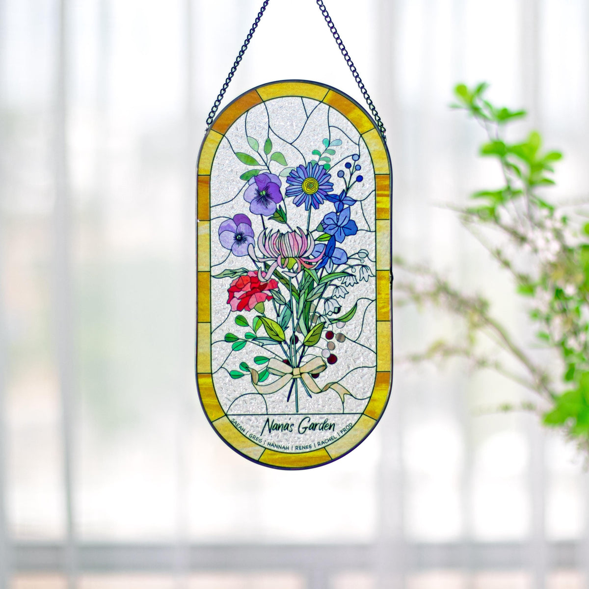 May include: Stained glass window art featuring a bouquet of colorful flowers in shades of red, purple, blue, and pink. The oval-shaped panel has a yellow border and is suspended by a black chain. The text "Nana's Garden" is visible at the bottom.