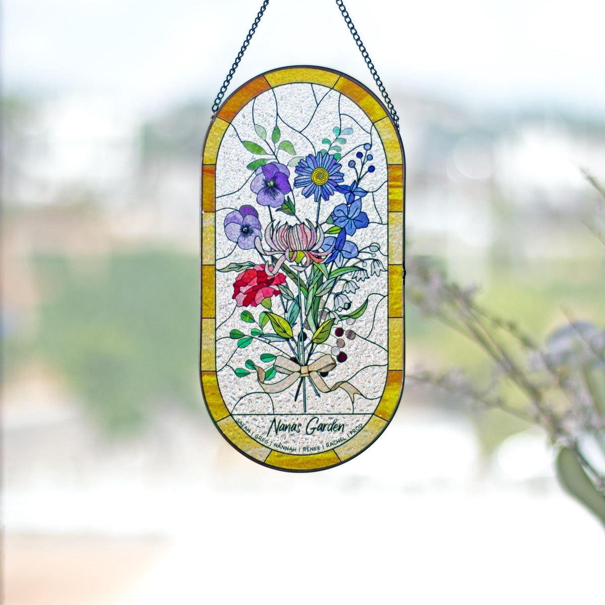 May include: Stained glass window panel featuring a bouquet of colorful flowers in shades of red, purple, blue, and pink. The flowers are tied with a beige ribbon. The panel has a yellow border and is suspended by a chain.