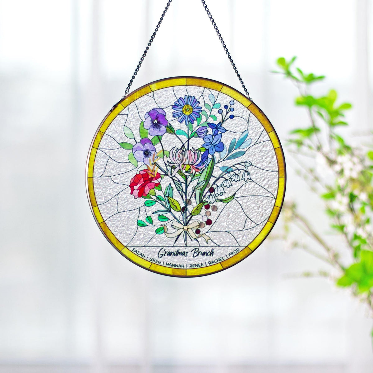 May include: A round stained glass window with a yellow border and a black chain for hanging. The window features a colorful floral bouquet with red, purple, blue, and white flowers. The text "Grandmas Brunch" is at the bottom.