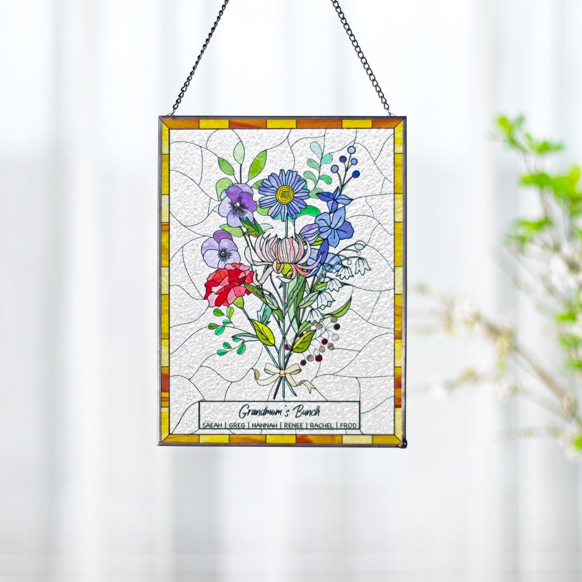 May include: Stained glass panel featuring a colorful floral bouquet with red, purple, blue, and white flowers. The panel has a yellow and orange border and is suspended by a chain. Text at the bottom reads "Grandma's Bunch" with names below.