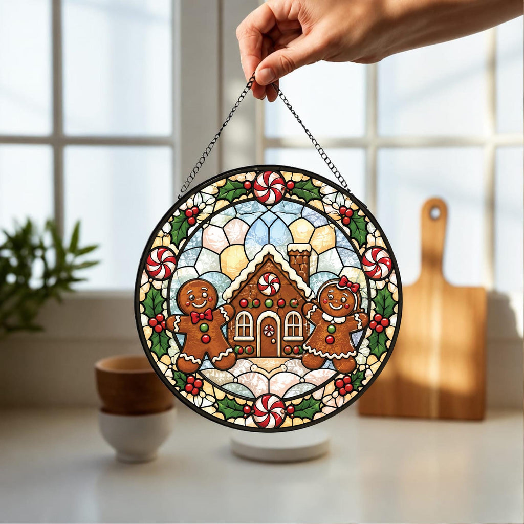 May include: A circular stained glass suncatcher featuring a gingerbread house at the center, flanked by two gingerbread figures. The border is decorated with red and white peppermint candies and green holly leaves, all held by a black metal chain.