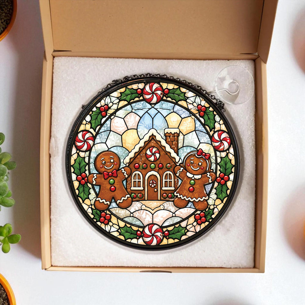 May include: A circular stained glass suncatcher featuring a gingerbread house, two gingerbread figures, and peppermint candies. The design is framed by green holly leaves and red berries, all enclosed in a black metal border with a suction cup.