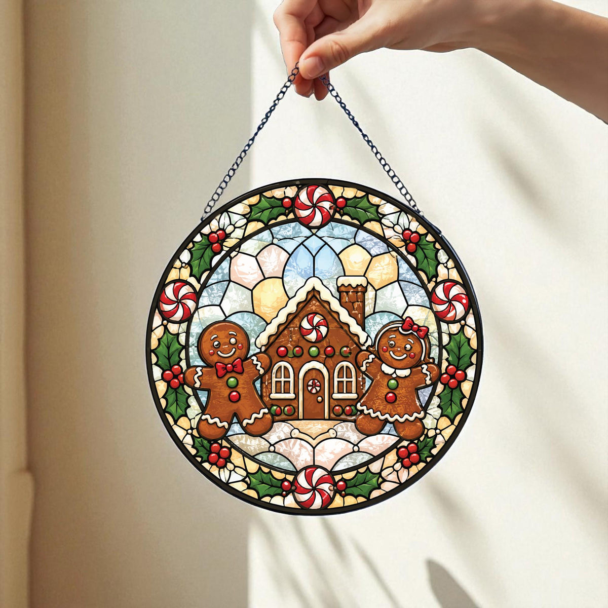 May include: A circular stained glass suncatcher featuring a gingerbread house in the center with a gingerbread person on each side. The border is decorated with green holly leaves, red berries, and red and white peppermint candies on a chain.
