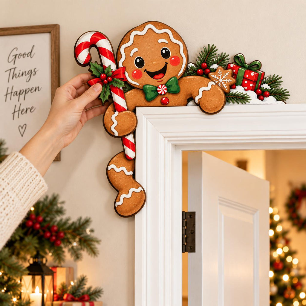 May include: A gingerbread man door corner decoration featuring a smiling face, a green bow tie, and a red and white candy cane. The ornament is accented with green pine branches, red berries, and a small gift box with a green ribbon.