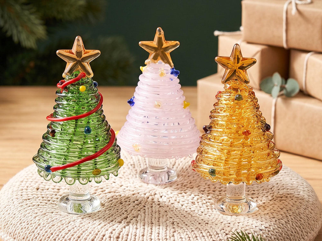 May include: Three glass Christmas tree figurines with clear glass stands and gold star toppers. One tree is green with a red spiral and colorful dots, one is pale pink with small star accents, and one is amber with scattered colorful glass beads.
