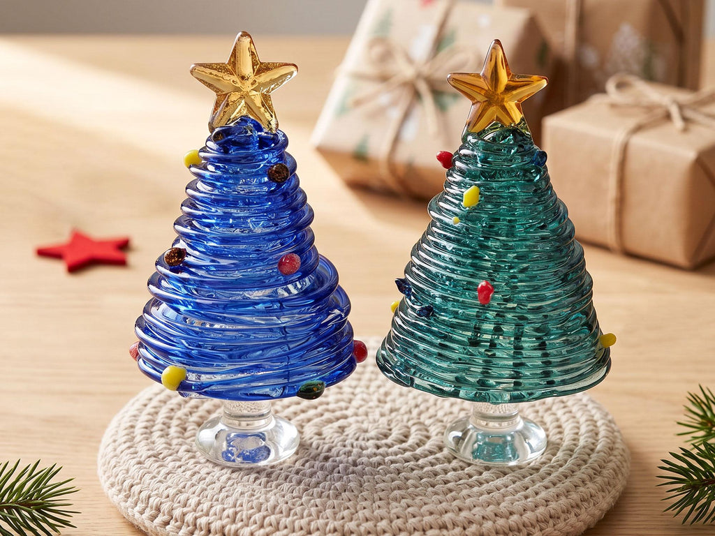 May include: Two glass Christmas tree figurines, one in cobalt blue and one in emerald green, each featuring a coiled glass design, small colorful glass bead ornaments, and a clear glass star topper, all supported by a clear glass pedestal base.