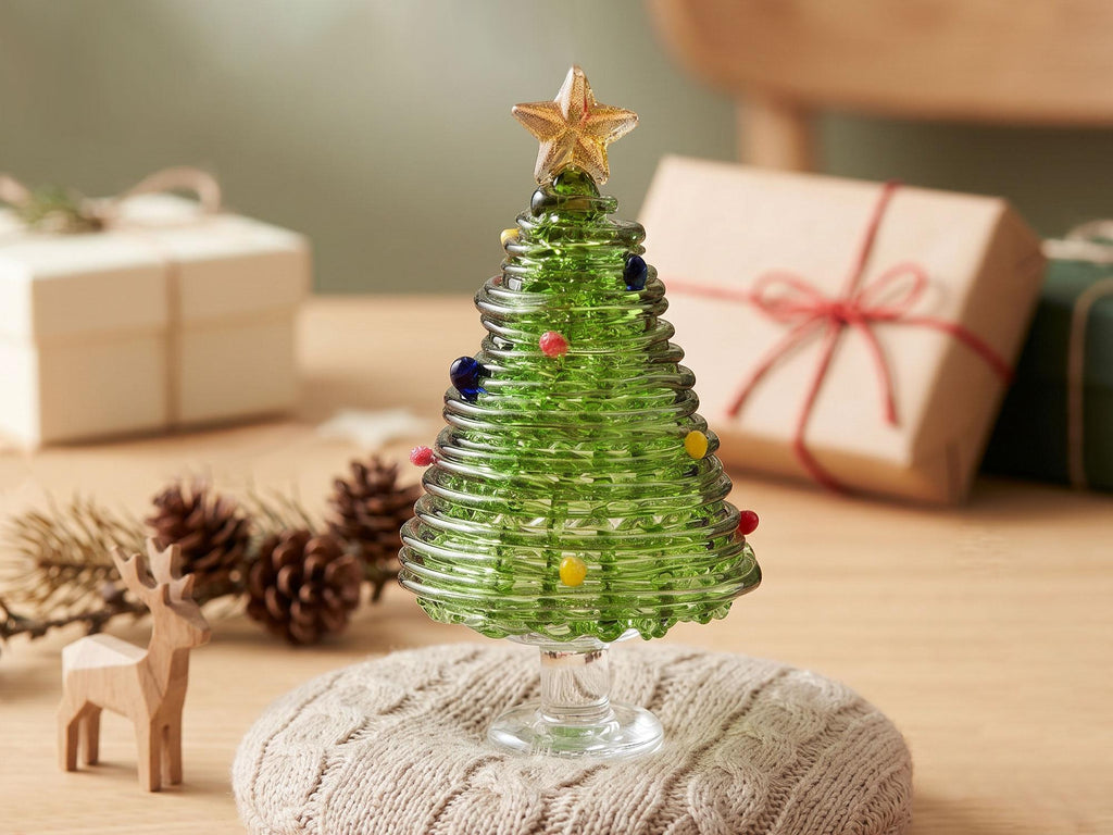 May include: A green glass Christmas tree figurine with a spiral design, featuring small colorful glass spheres as ornaments and a clear glass star topper. The tree stands on a clear glass pedestal base, showcasing a translucent finish.
