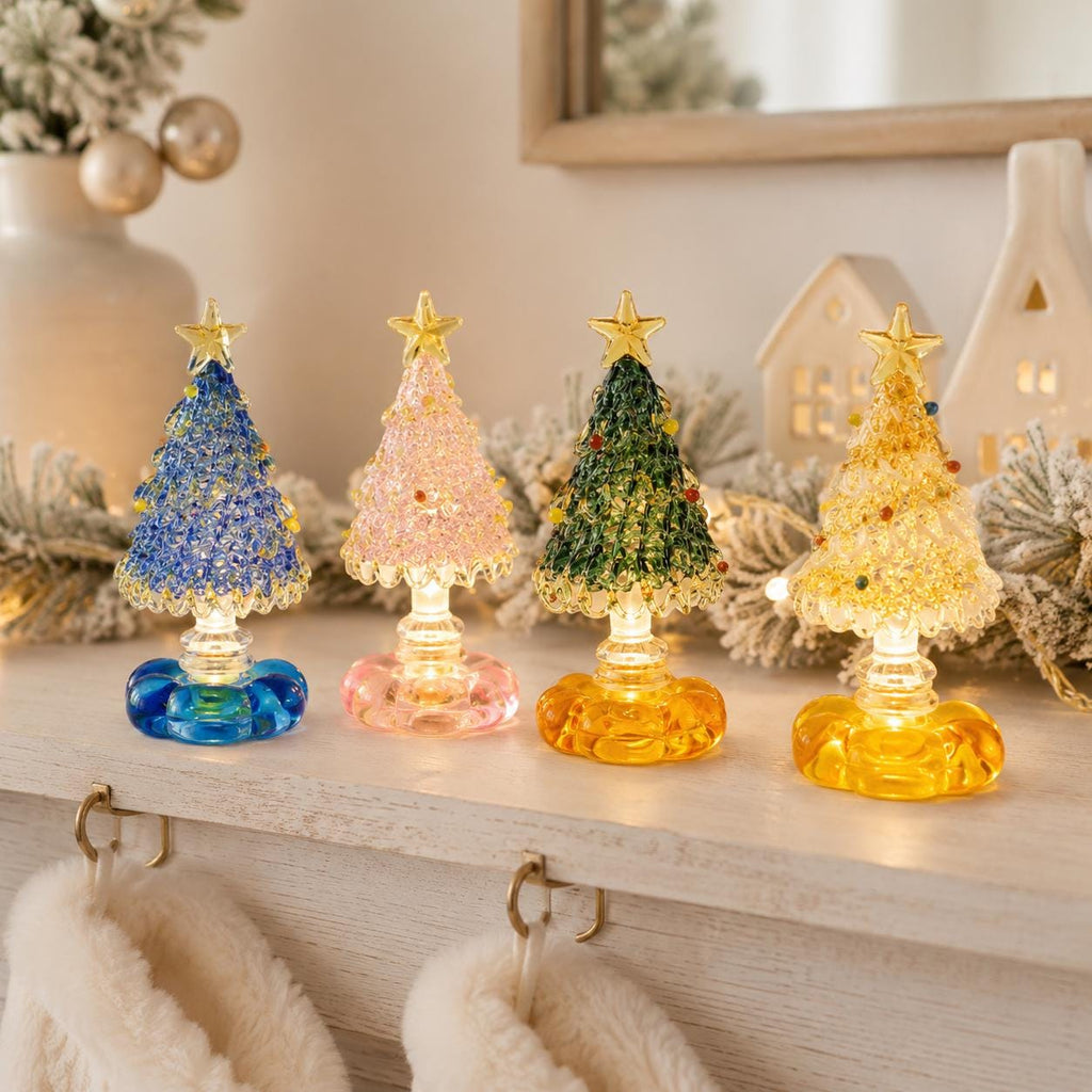 May include: Four miniature glass Christmas tree figurines with textured, beaded surfaces and a star topper. Each tree sits on a clear, illuminated base. The trees are colored in blue, light pink, green, and yellow, featuring small embedded accents.