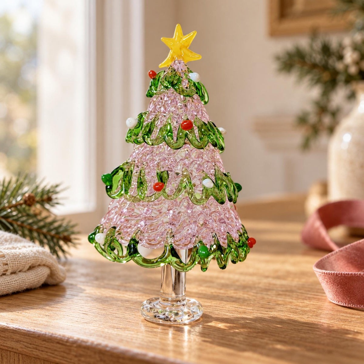 May include: A decorative glass Christmas tree figurine featuring a textured pink conical body wrapped in swirling green glass garlands. The tree is adorned with small red and white glass spheres and topped with a bright yellow glass star.