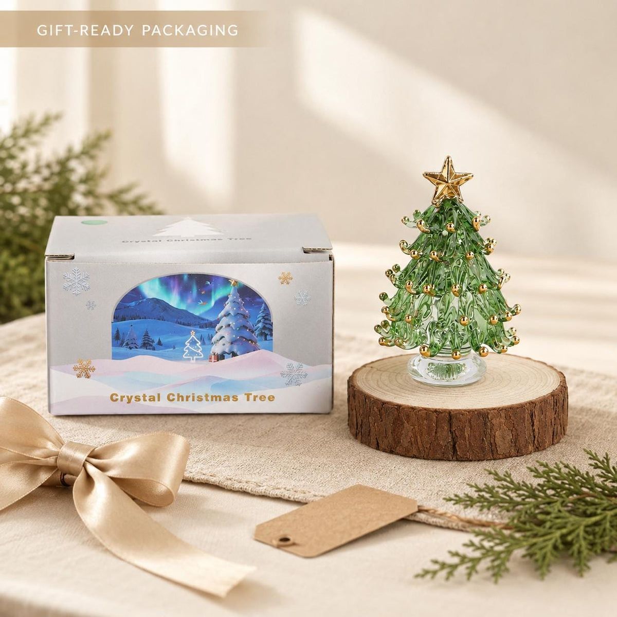 May include: A green glass Christmas tree figurine with gold accents and a gold star topper, displayed on a round wooden base. Beside it sits a rectangular box labeled Crystal Christmas Tree, featuring an illustration of a snowy landscape.
