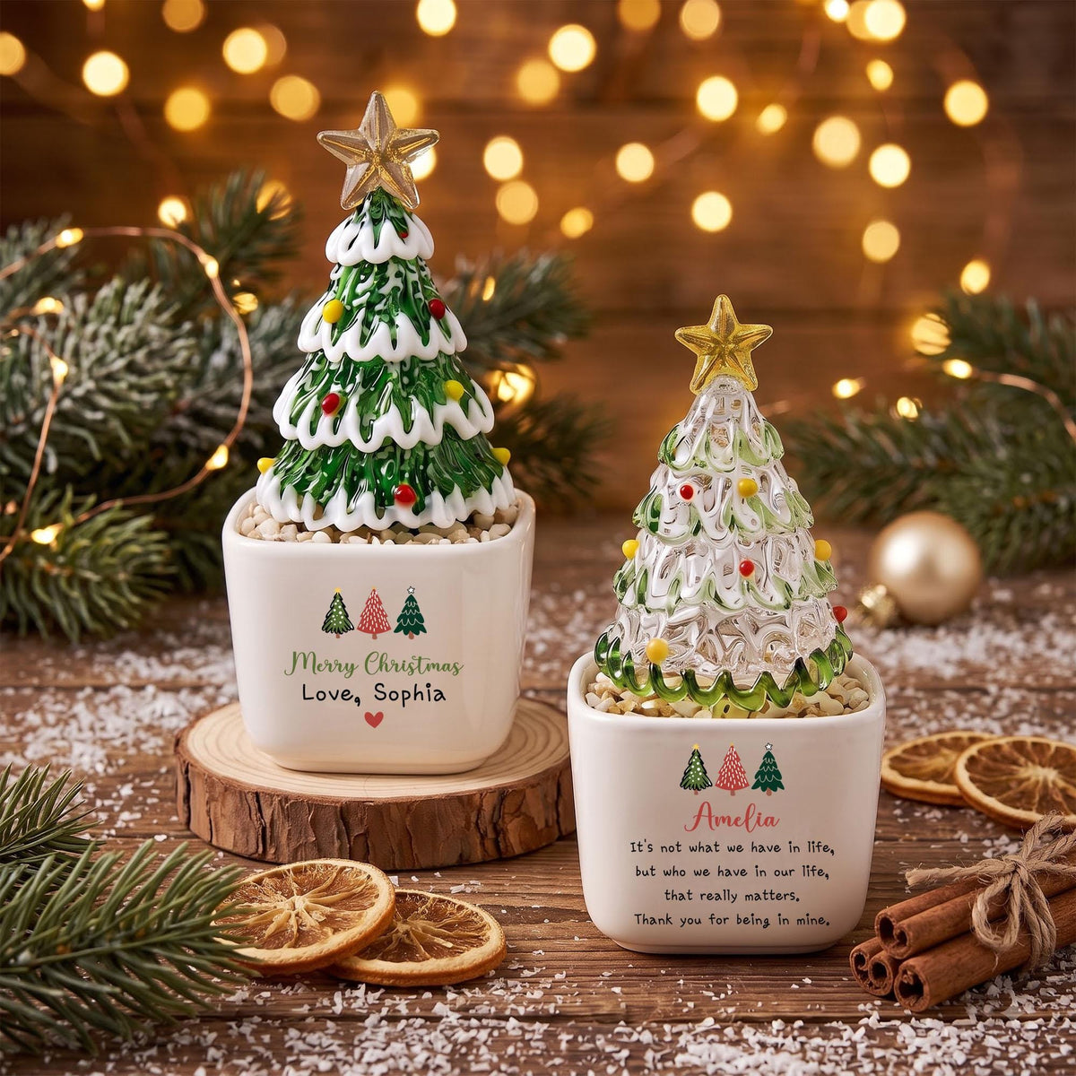 May include: Two ceramic square planters containing glass Christmas tree ornaments with gold stars on top. The left planter features green trees and text reading Merry Christmas Love, Sophia. The right planter features text reading Amelia and a quote.