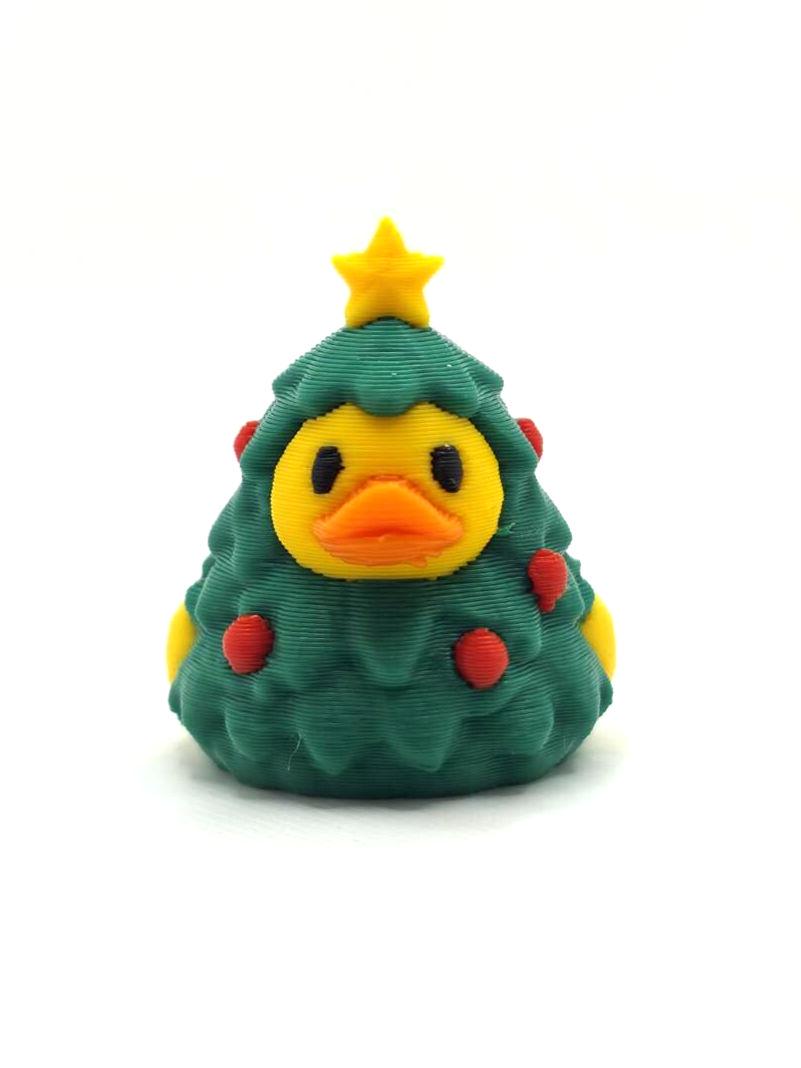 May include: A 3D printed duck figurine wearing a dark green Christmas tree costume. The duck has a yellow face, orange beak, and black eyes. The tree costume features a yellow star on top and small red circular ornaments scattered throughout.