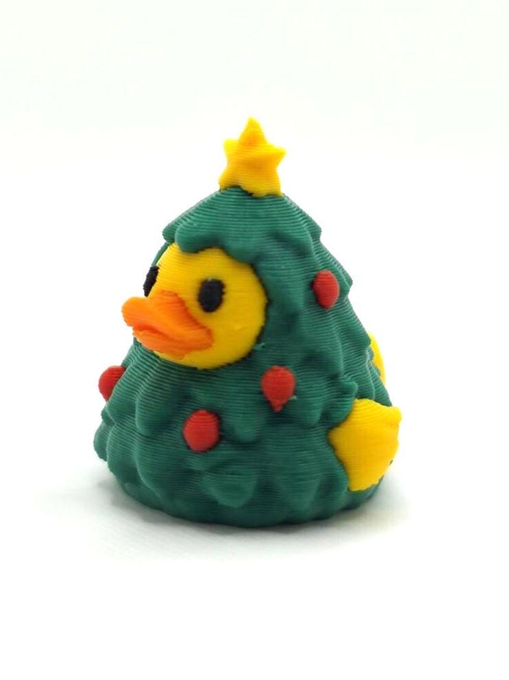 May include: A 3D printed rubber duck figurine shaped like a Christmas tree. The duck has a yellow head, an orange beak, and black eyes. The body is green with red circular ornaments and a yellow star on top, with yellow wings visible on the side.