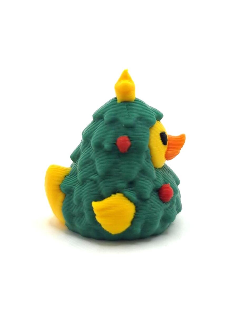 May include: A 3D printed rubber duck figurine shaped like a Christmas tree. The duck has a dark green textured body, a bright yellow head, wings, and tail, an orange beak, and small red circular ornaments embedded on the green surface.