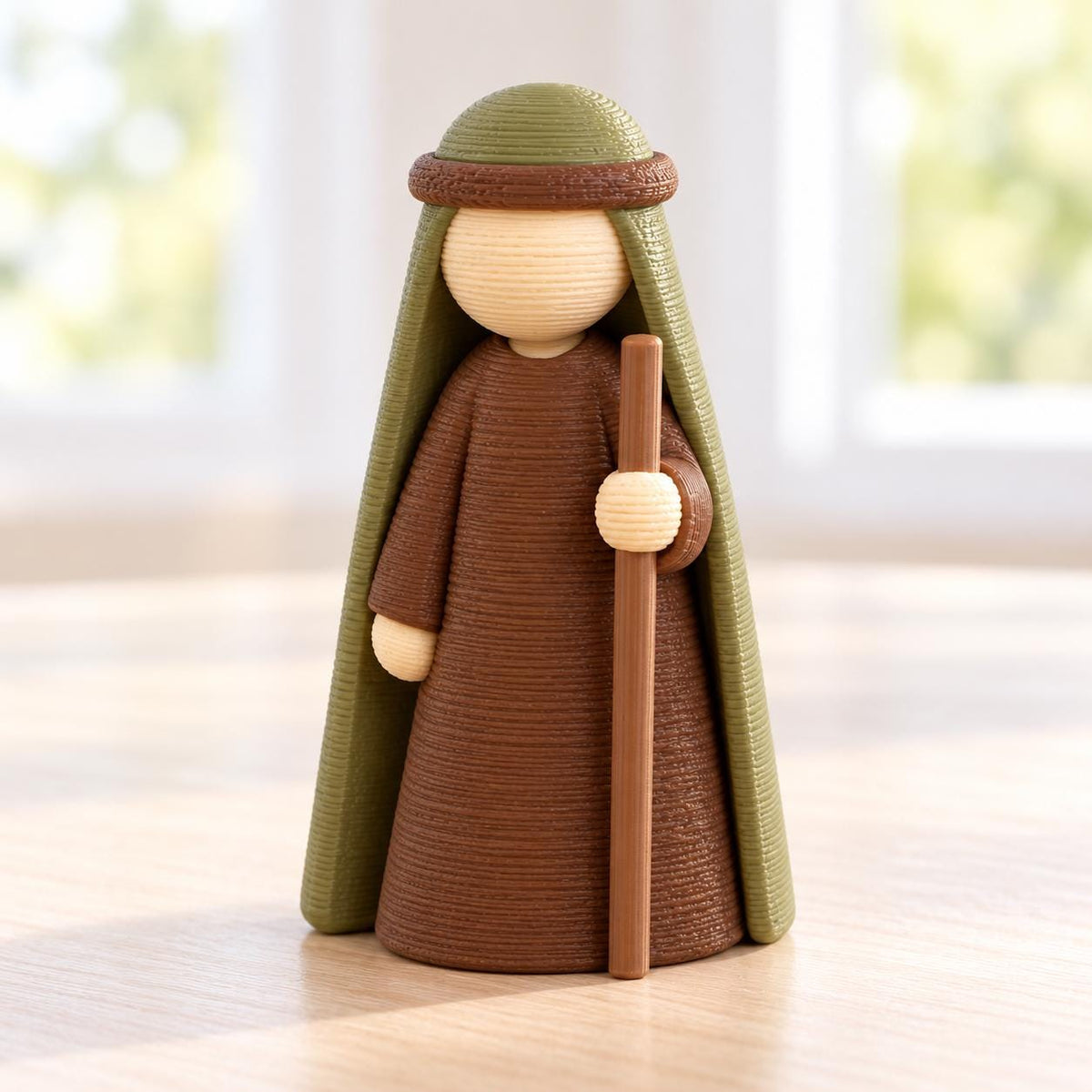 May include: A small figurine of a person wearing a brown robe and a green head covering. The figure has a smooth, round, light-colored head and holds a long, thin brown staff in one hand. The entire object features a textured, layered surface.