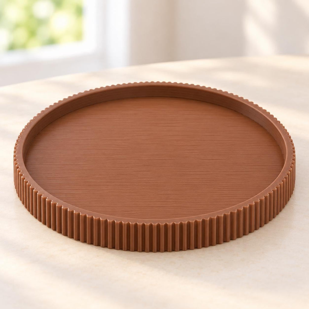 May include: A circular, medium-brown tray featuring a flat, smooth base and a raised, vertically ribbed outer edge. The tray has a consistent, solid color throughout and a clean, simple design with a defined rim that encircles the entire perimeter.
