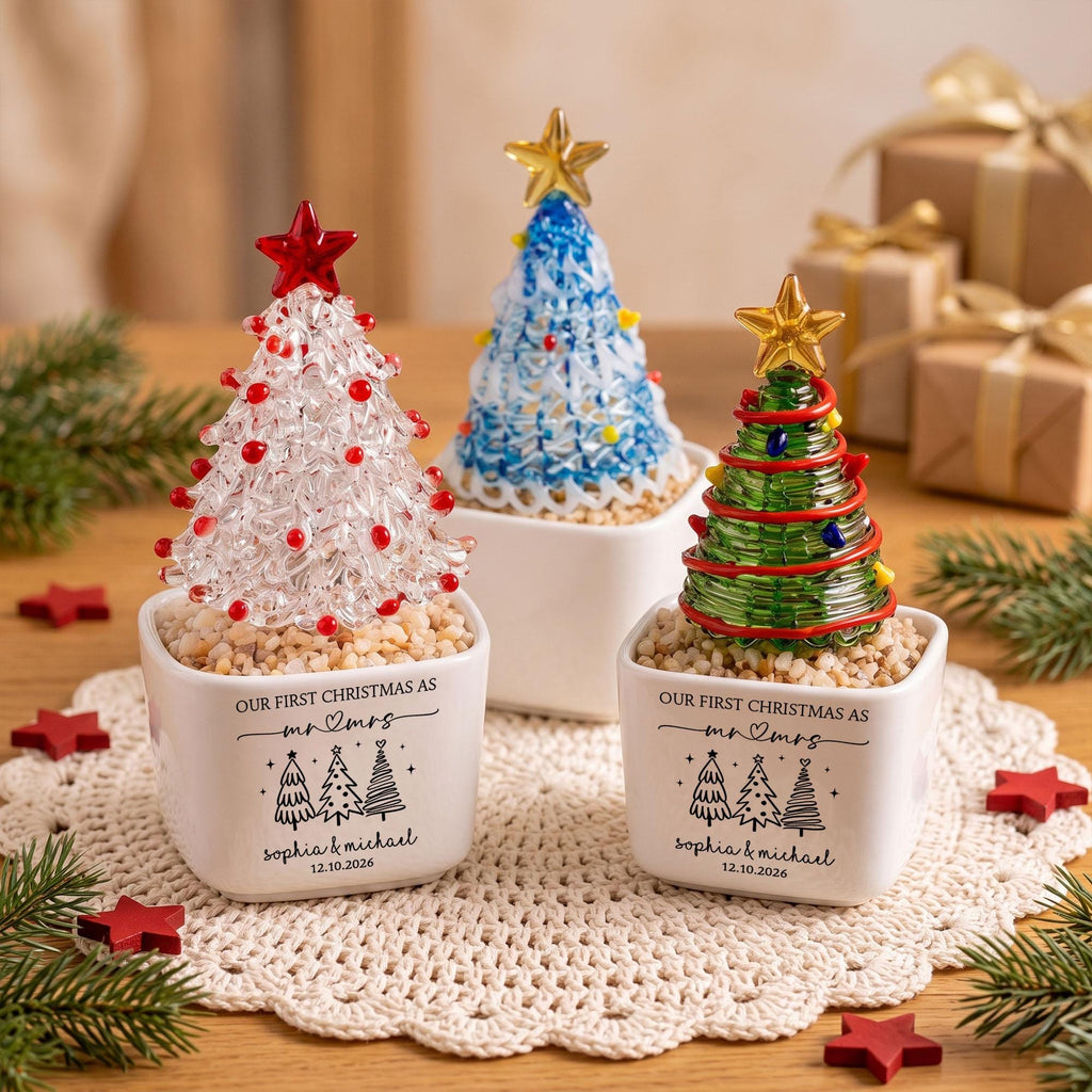 May include: Three glass Christmas tree ornaments in white square planters. Each tree features a star topper and colorful accents. The planters are printed with the text "OUR FIRST CHRISTMAS AS mr & mrs", "Sophia & Michael", and "12.10.2026".
