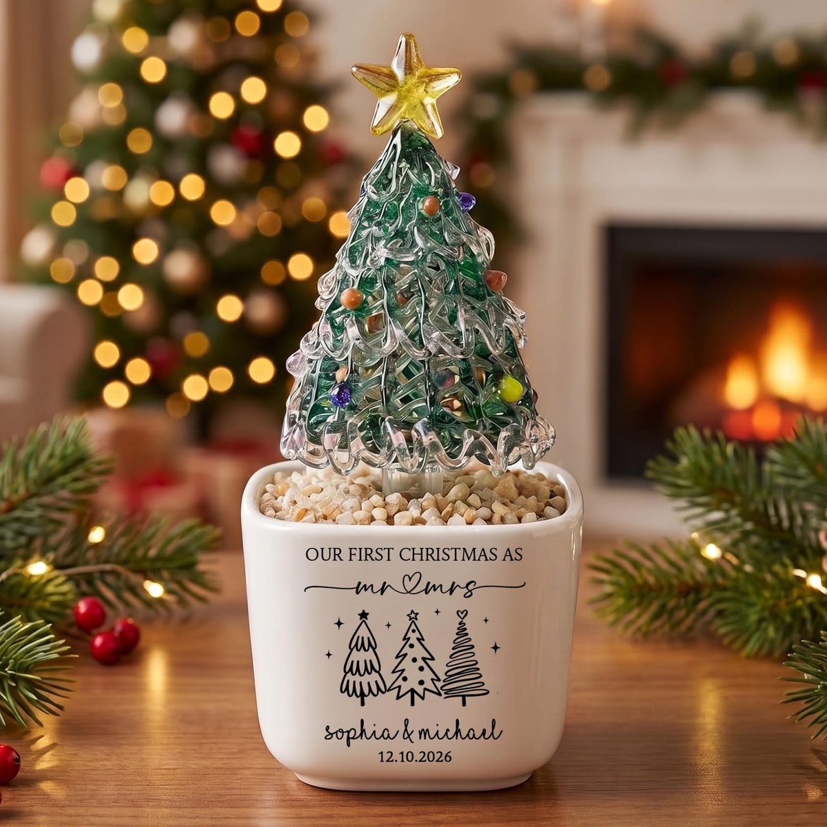 May include: A glass Christmas tree figurine with a yellow star topper and colorful glass ornaments, set in a white ceramic planter filled with small stones. The planter features the text "OUR FIRST CHRISTMAS AS mr & mrs", "sophia & michael", and "12.10.2026" with three tree illustrations.