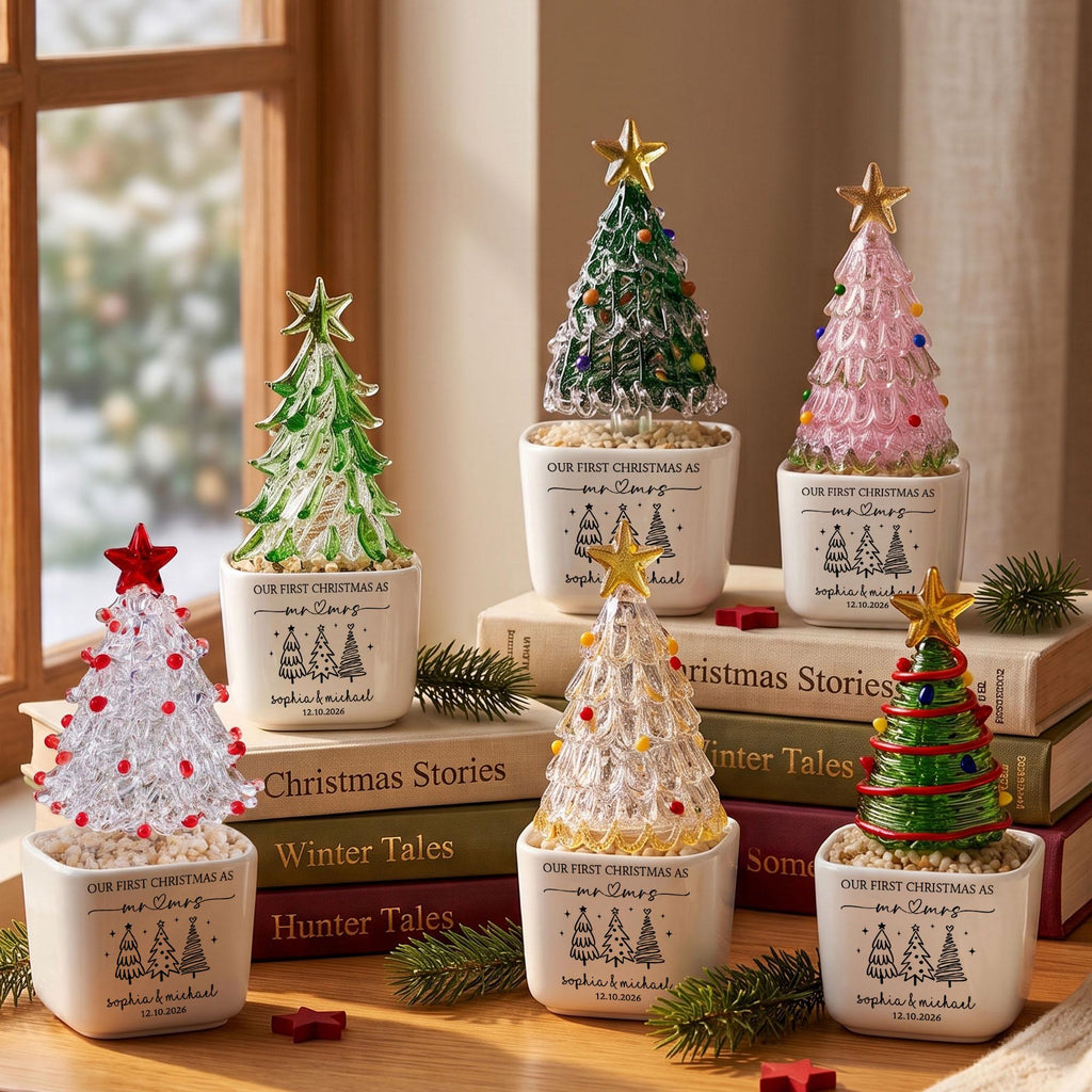 May include: Six glass Christmas tree figurines in white ceramic pots. Each tree features a gold or red star topper and colorful glass ornaments. The pots are printed with the text Our First Christmas as mr & mrs, Sophia & Michael, 12.10.2026.